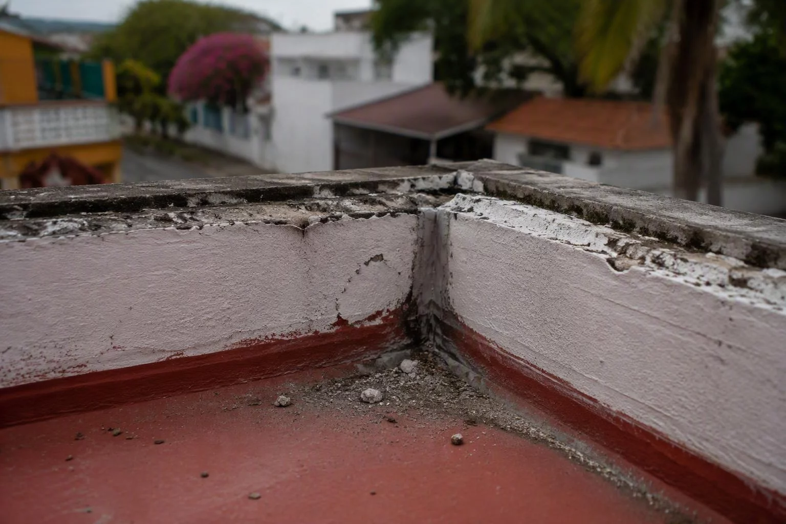 Esquina de pretil de azotea con sellador viejo y polvo acumulado en la base